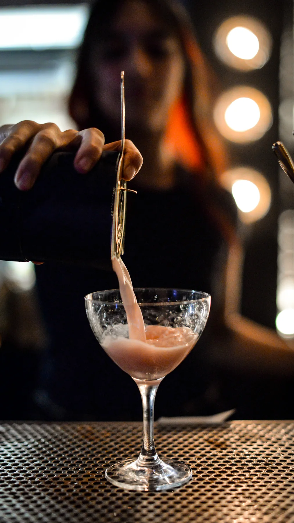 A bartender pours a pink cocktail into a coupe at BlackSheep