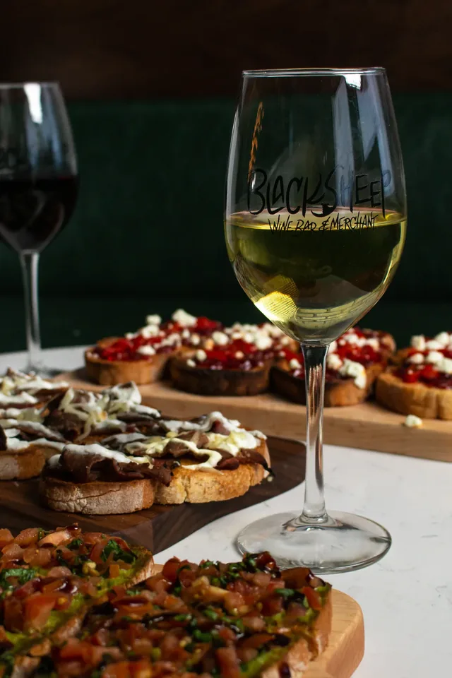 A glass of white wine beside bruschetta boards at BlackSheep