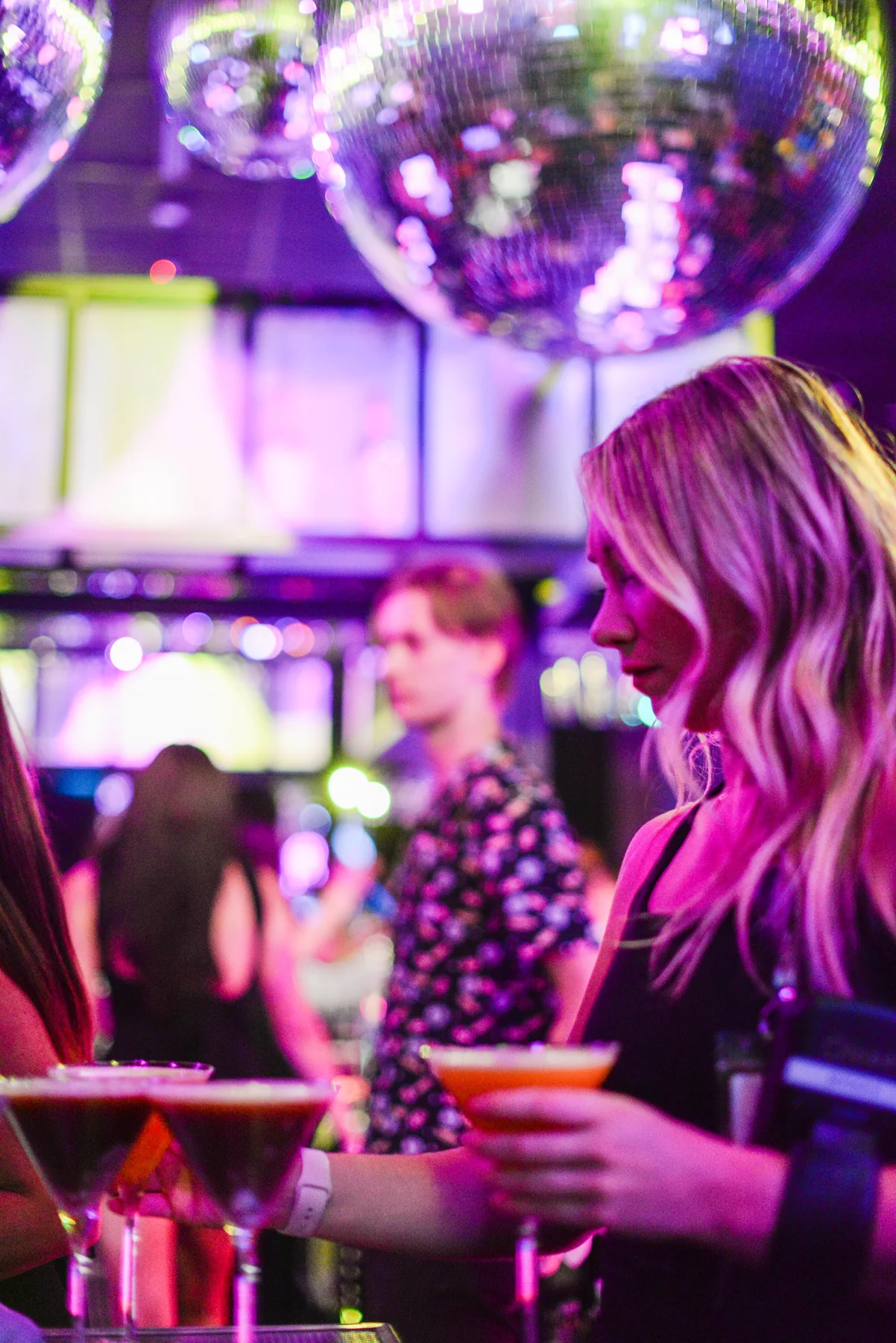 A bartender serves cocktails beneath a disco ball at Lola’s Liquors